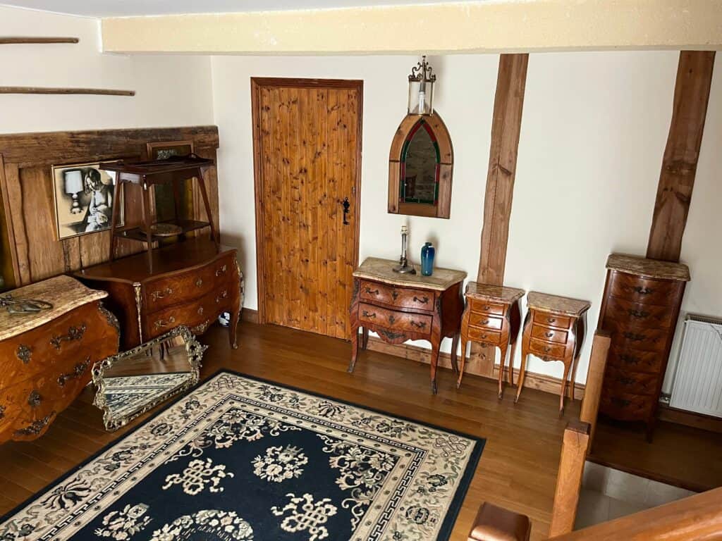 A room curated by Essex antique dealer, Village Vintage, featuring antique furniture like chests of drawers, small tables, hanging mirrors and a patterned rug.